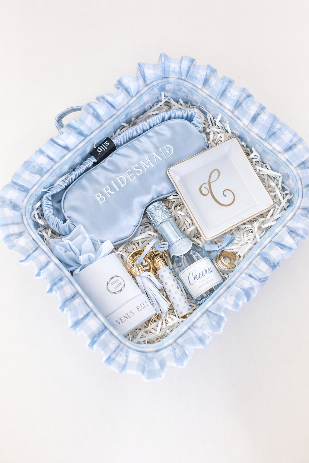Blue ruffled HOLLIS travel bag styled as a bridesmaid gift box with embroidered “Bridesmaid” sleep mask and bridal party accessories.